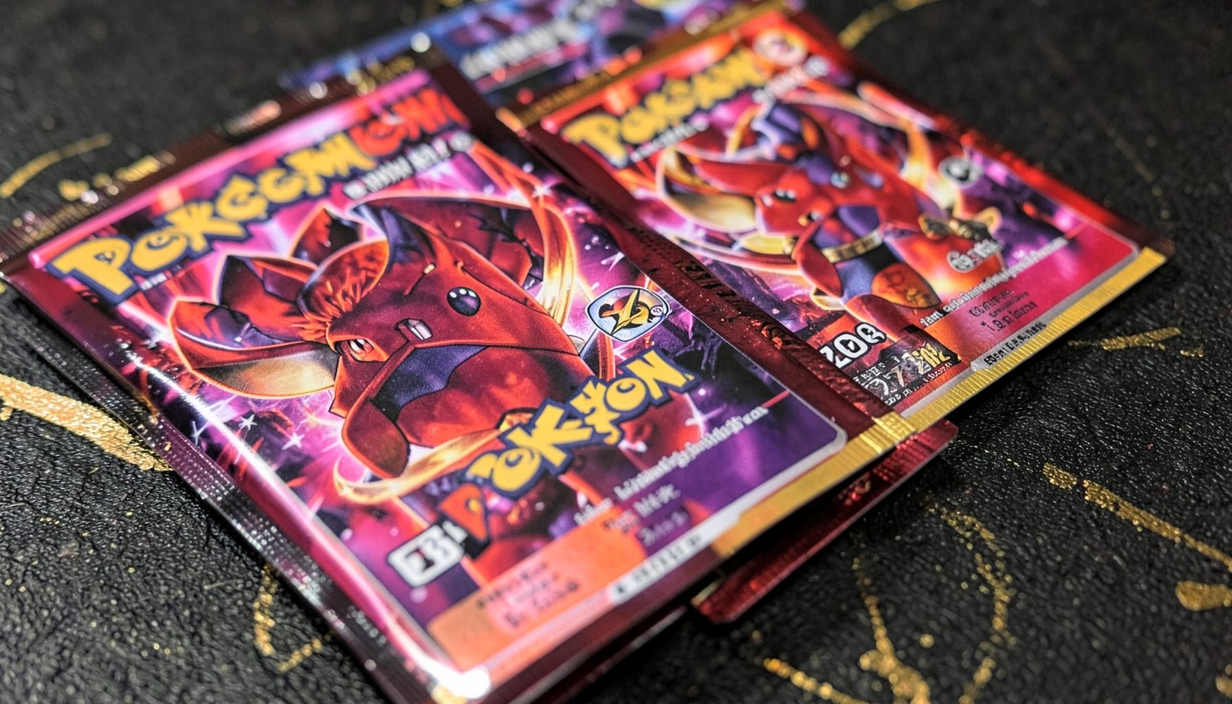 Close-up of glossy Pokémon trading card booster packs in rich scarlet and violet tones, arranged on a dark textured surface with subtle gold foil accents