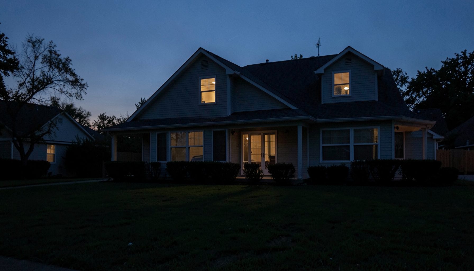 Suburban house at twilight with a single lit upstairs window, long shadows stretching across the lawn, quiet unease